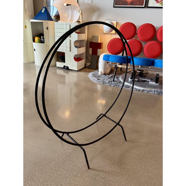This mid-century modern fireplace log holder, produced circa 1950–1960, is constructed from solid wrought iron with a...