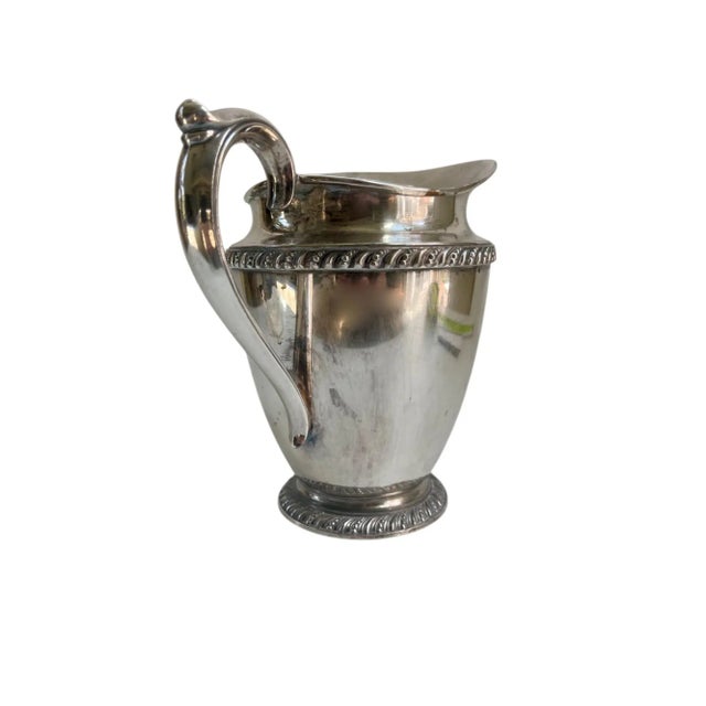 Vintage pitcher in a classic shape with a handle and spout, with ornate rope detailing along the rim. Designed for serving...