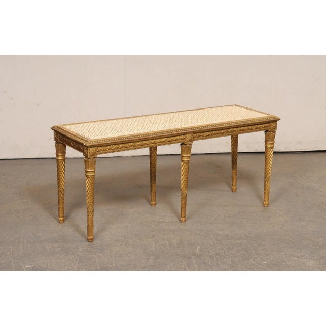 A French carved and gilt wood bench with cane seat from the early 20th century. This antique backless bench from France...