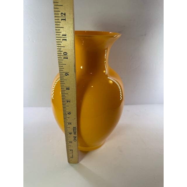 This striking 11.5-inch tall hand-blown cased glass vase features a vibrant, high-gloss yellow exterior with a contrasting...