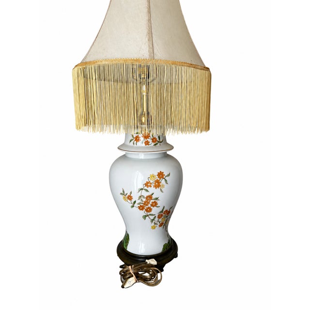 A striking chinoiserie table lamp featuring a glossy white ceramic ginger jar body decorated with orange and yellow...