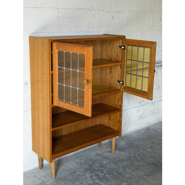 This versatile display cabinet features upper glass doors with leaded details, open lower shelving, and slender tapered...