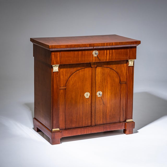 Two-door Empire cabinet with a drawer and flanking bronze pilasters. The mounts are likewise executed in bronze. The doors...