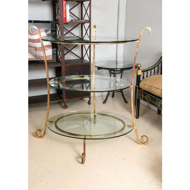 Three-tier glass and gilt metal etagere stand. Warm toned gilt metal curved legs that connect three circular bases that...