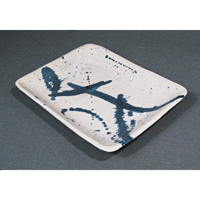 A quietly striking studio pottery tray with a pale speckled ground and bold cobalt-blue brushwork, combining painterly...