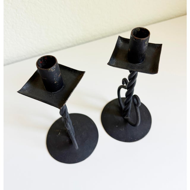 A sculptural pair of wrought iron candle holders featuring a distinct twisted stem design and decorative spiral base...