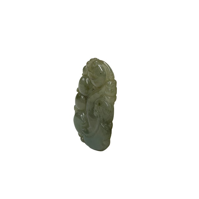 This elegantly carved pendant is crafted from a translucent, celadon-green stone—likely jadeite—featuring a mottled...
