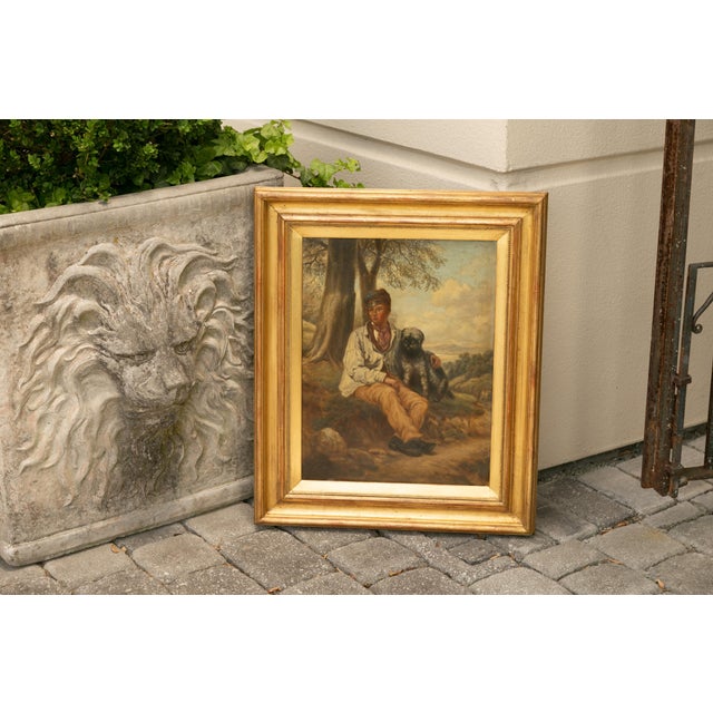 An English oil on canvas painting from the late 19th century depicting a boy sitting with his dog, in antique giltwood...