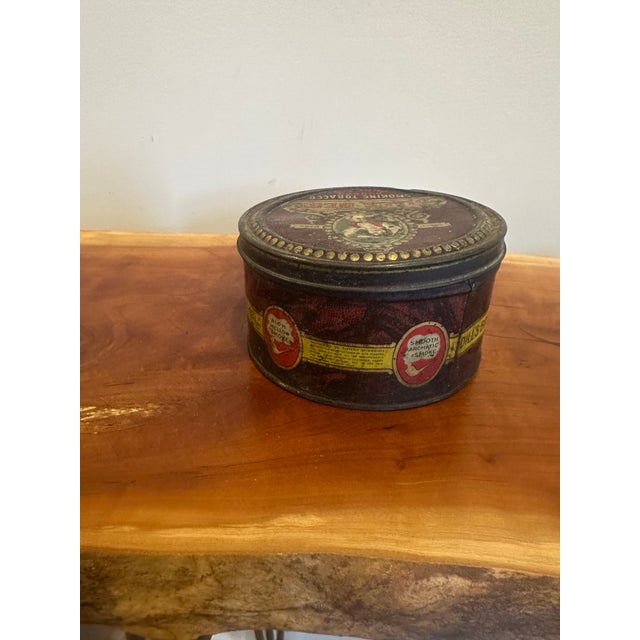 Authentic vintage tobacco tin featuring classic advertising graphics and rich, aged patina. The deep brown tones, gold...