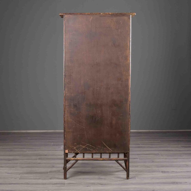 A bamboo cabinet in a dark brown finish, with two glass doors, each fitted with an X-strut bamboo motif at the top and...