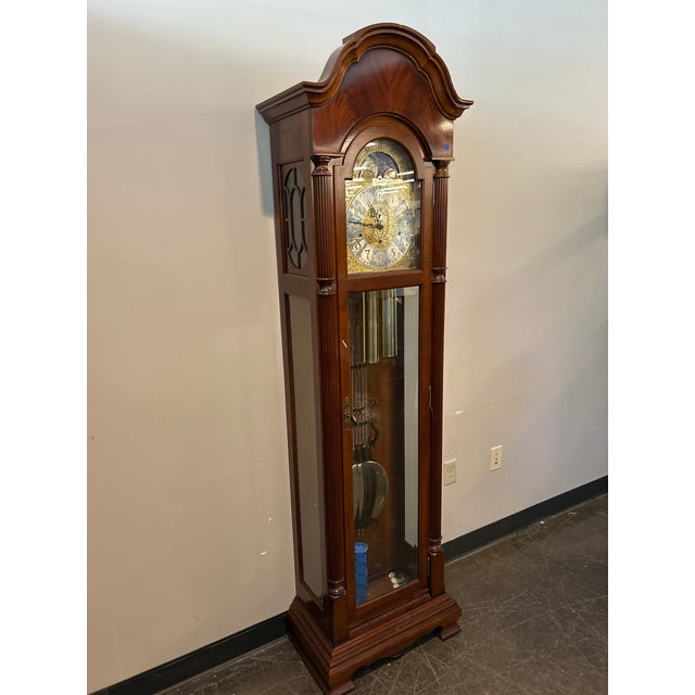 A stately mahogany grandfather clock by Sligh, featuring an ornate gold-toned face with moon dial, decorative pendulum,...