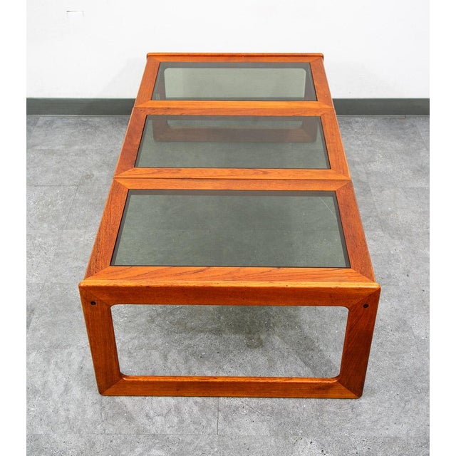 Clean solid teak coffee table by Komfort Mobler. Smoked glass top surface on the three center panels. Unique and extremely...