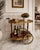 Elegant vintage two-tier tea and serving cart featuring warm mahogany-tone wood, decorative floral detailing, turned wood...