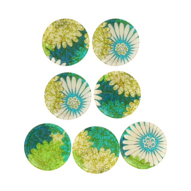 Set of seven vibrant 1960s fiberglass drink coasters, each featuring a different abstract floral design in cheerful shades...
