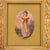 An ornate gold-tone frame surrounds a charming vintage illustration of a young girl holding a white cat. Dressed in a red...