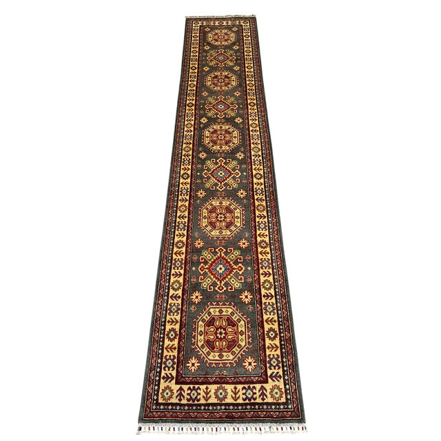 This long Kazak-style wool runner pairs a charcoal gray field with a cream border and a rhythmic row of geometric...