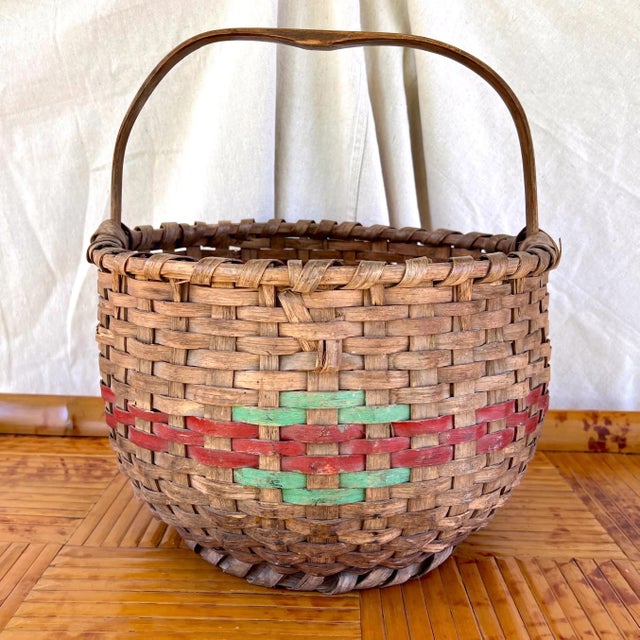 A large American hand-woven oak splint gathering basket with a bent oak handle. Red and green painted decoration on front...