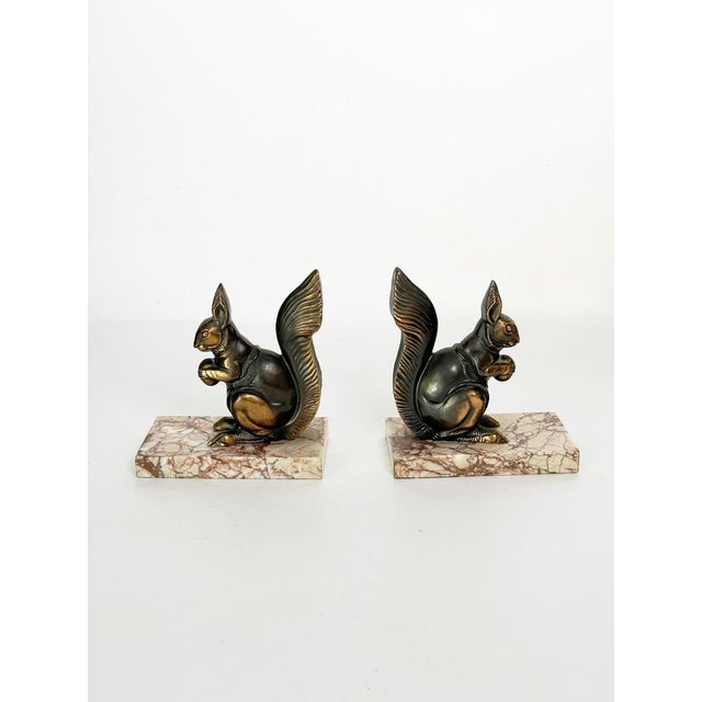 A charming pair of vintage bookends featuring patinated metal squirrel sculptures with a bronze finish, set upon veined...