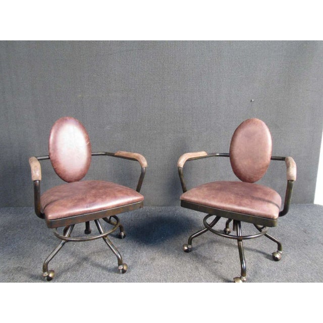 These rustic vintage rolling chairs feature a solid metal construction, swiveling seat, upholstered backrest and seat as...