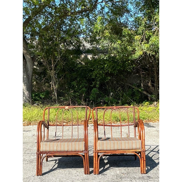 Add a touch of breezy elegance to your space with this stunning pair of vintage bent loop rattan lounge chairs. With...