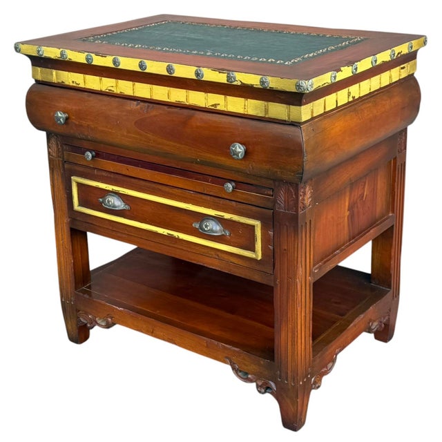 An exceptional vintage GuildMaster accent chest featuring warm wood tones, hand-painted gold trim, and a green leather...
