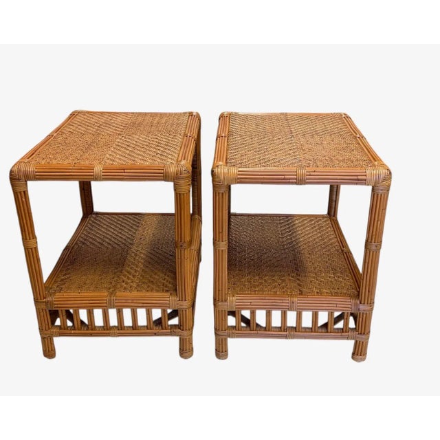 Pair of tiki side tables made from pencil reeds and caning. The legs and edges of the top and shelf are reeds bound with...