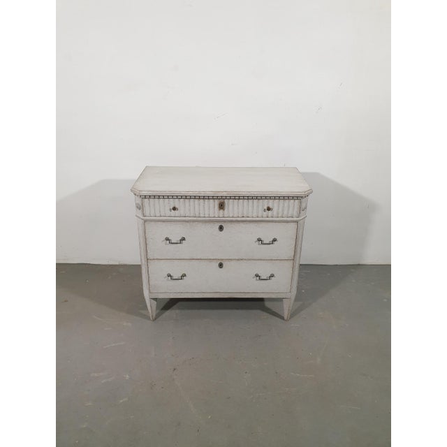 A Swedish Gustavian style chest from circa 1860 with three drawers, light gray painted finish, reeded accents, dentil...
