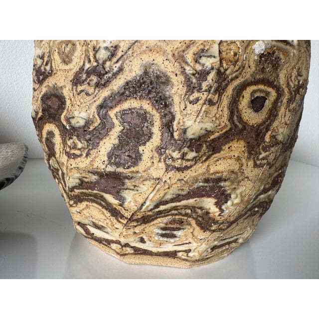 This 1980s vintage studio pottery vase showcases a striking marbled agateware design, blending earthy beige, cream, and...