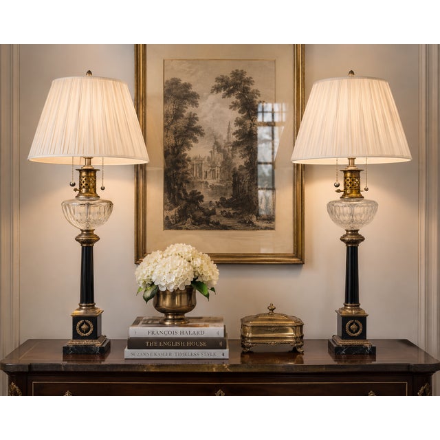 A striking pair of neoclassical Empire-style table lamps, showcasing a sophisticated blend of crystal, black marble, and...