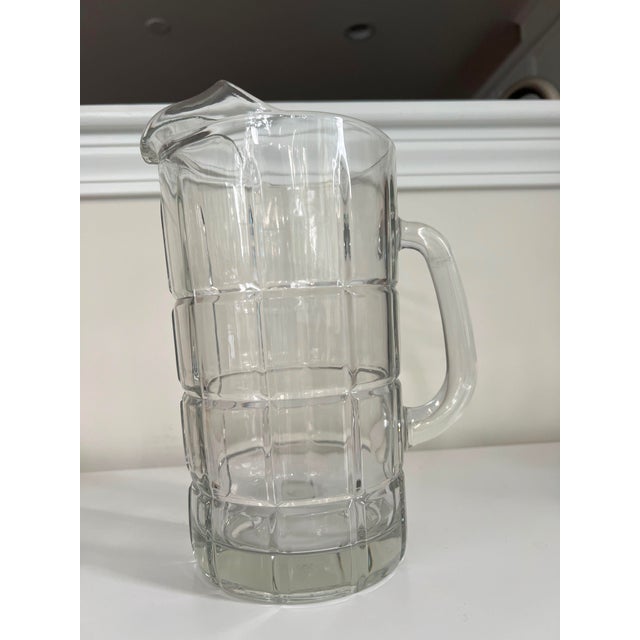 This vintage Anchor Hocking mid-century water pitcher features a bold, geometric grid cut-glass pattern that reflects...