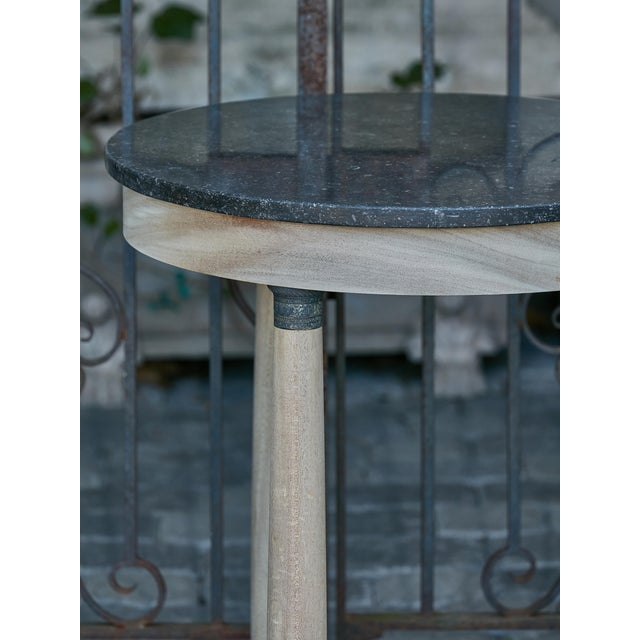 A French Empire style bleached wood side table from the 19th century with black marble top, three column legs, in-curving...
