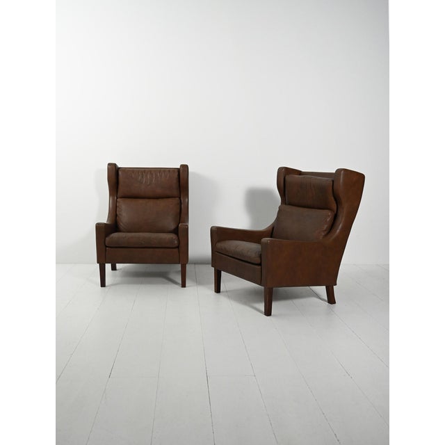 Pair of armchairs, likely Danish, from the 1950s, in dark brown leather, with high backs and removable cushion covers....