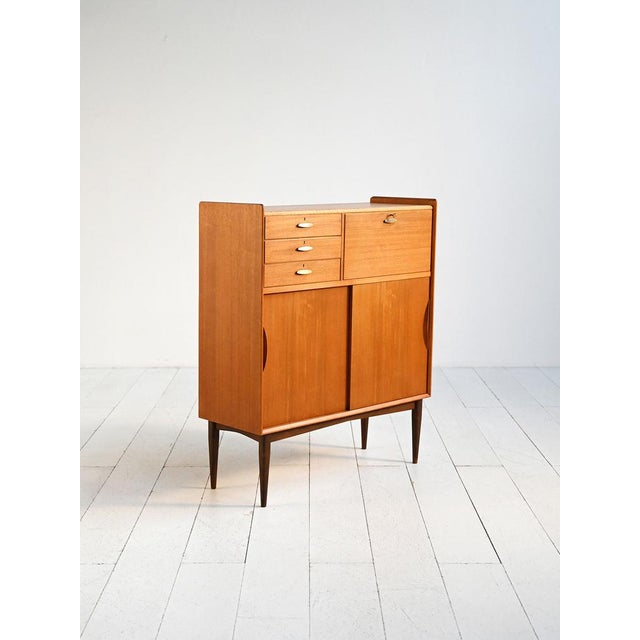 Teak cabinet with three drawers, sliding doors, brass handles, and a dark-stained beech base. Danish production,...