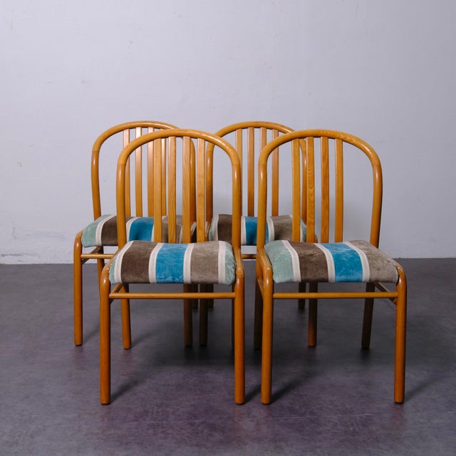 Beautiful set of 4 wooden dining chairs with vertical slatted backrests and padded seats upholstered in blue, brown, and...