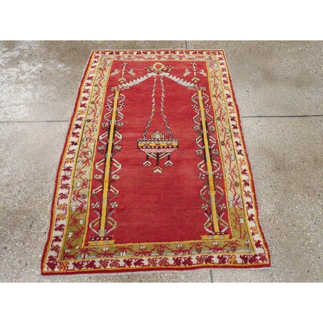 An antique Turkish Ghiordes throw rug. An elaborate lamp is suspended by two chains in an open cochineal red niche with...