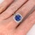 A tanzanite glows in a deep violet-blue at the heart of this solid 14K white gold ring, flanked by thirty-two earth-mined...
