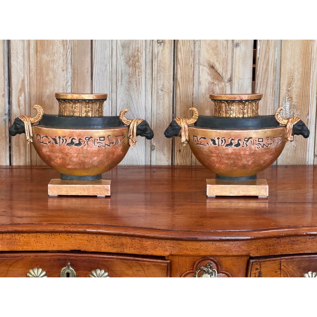 A pair of Neoclassical painted and gilt flatback urn ornaments in the Egyptian taste — each half-round bowl with black...
