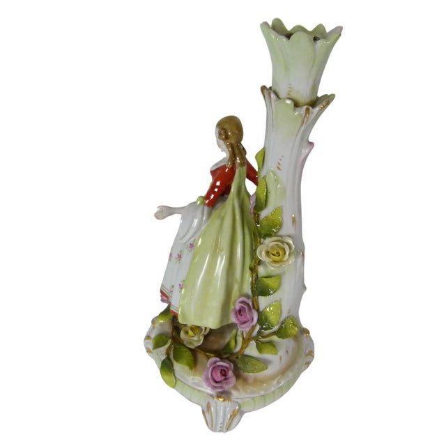A Dresden-style figural single candlestick depicting an 18th-century courtly Lady standing against a floral tree trunk...