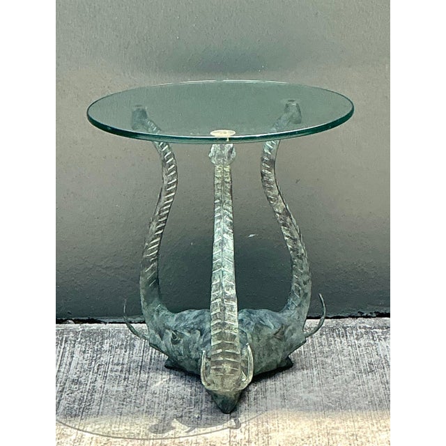 This striking side table features a captivating figural base composed of three expertly cast elephants in a tripod...