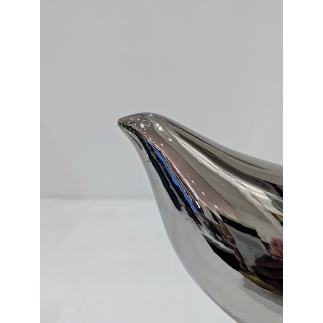 Decorative ceramic bird sculpture distributed by Raymor, featuring a reflective silver glaze and mounted on a white marble...