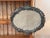 An oval tole trade sign with a continuous wreath of hand-cut and painted metal laurel leaves surrounding a plaster ground,...