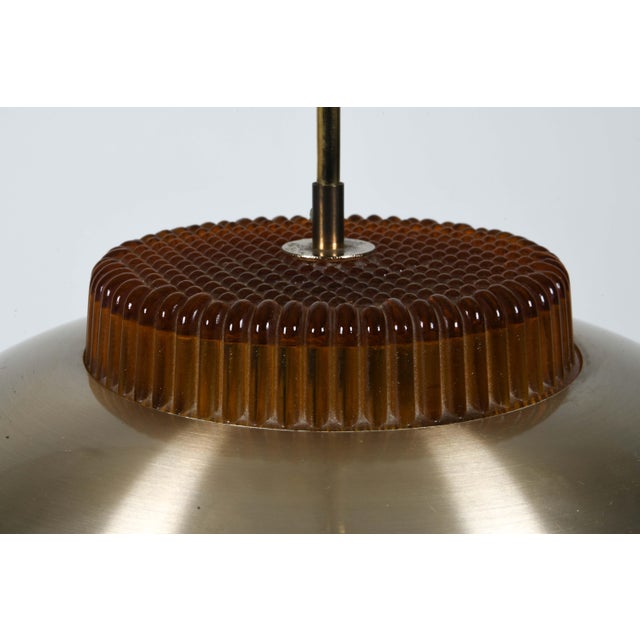 A sculptural Danish pendant from the 1970s, combining brushed aluminum, amber glass, and a concentric diffuser system...