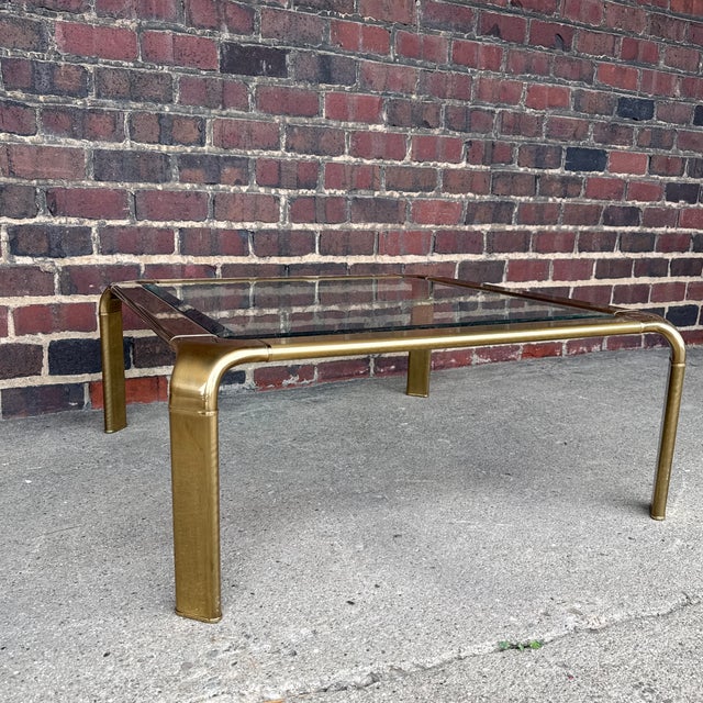 Mid-Century Modern brass and glass coffee table by Widdicomb, featuring a substantial brass frame with softly rounded...