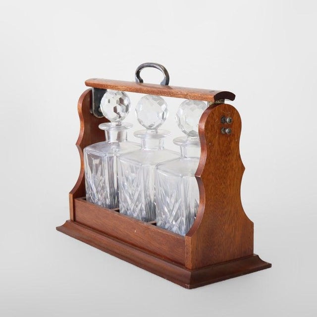 An antique oak tantalus set featuring three finely crafted cut glass spirit decanters, dating to approximately C1920. This...