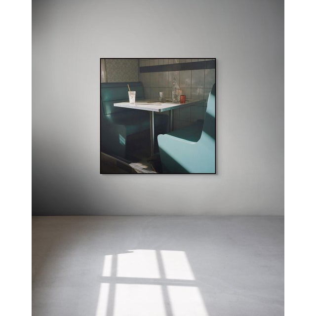 Ice Cubes and Paper Straws by Mark Forbes transforms an empty diner booth into a study in stillness and fading light....