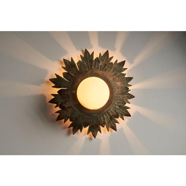 Decorative wall or ceiling light with a radiating sunflower-like metal frame and textured glass diffuser. The fixture is...