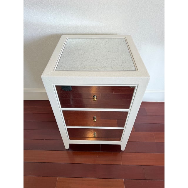 Elegant Made Goods nightstand featuring a faux shagreen textured frame in a soft ivory finish with inset antique mirror...