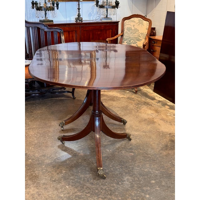 Description: Mahogany dining table with an oval top and a single leaf (leaf shown). Raised on two pedestals, each ending...