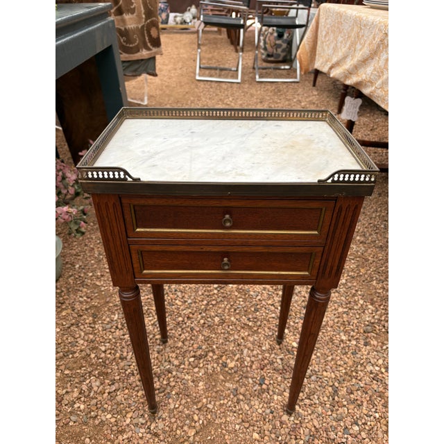 French Louis XVI style mahogany bedside table, 20th c., having inset marble top with pierced gilt-metal three-quarter...