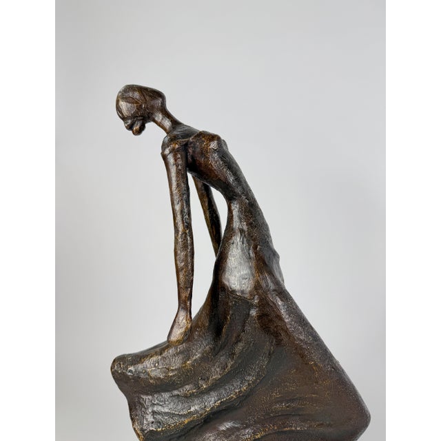 This modern bronze sculpture captures a stylized female figure in motion, her flowing dress sweeping outward as if caught...